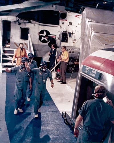 Posádka Apolla 12 (Conrad, Gordon, Bean) v respirátorech míří do karanténního přívěsu na palubě USS Hornet (NASA).