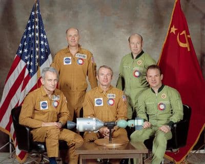 Společný portrét posádek Apolla–Sojuz: tři američtí astronauti a dva sovětští kosmonauti s vlajkami USA a SSSR.