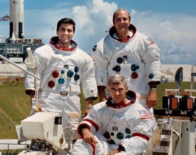 Official portrait of the Apollo 17 prime crew: Eugene Cernan, Ronald Evans, and Harrison Schmitt, with a Lunar Roving Vehicle trainer and the Saturn V in the background, 10 October 1972.