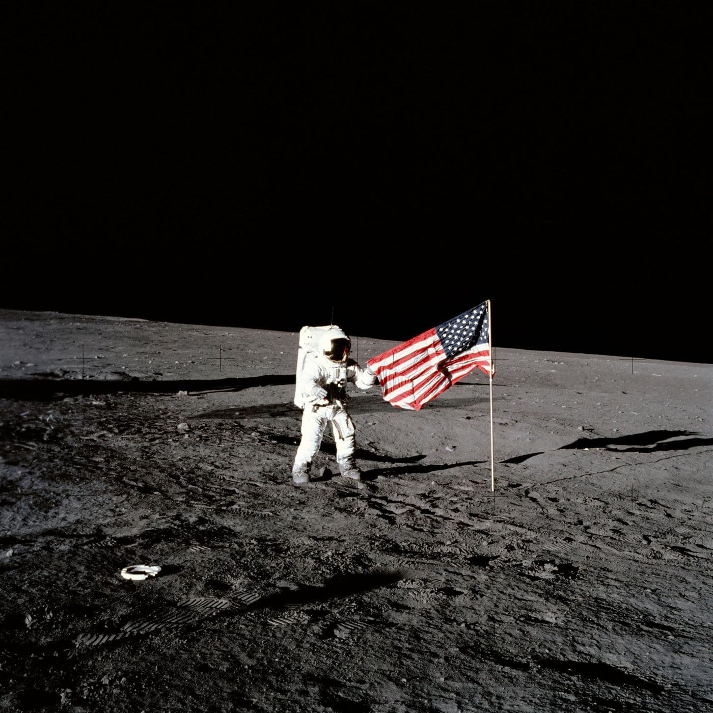 Astronaut Apolla 12 u vztyčené vlajky USA na povrchu Měsíce (NASA).