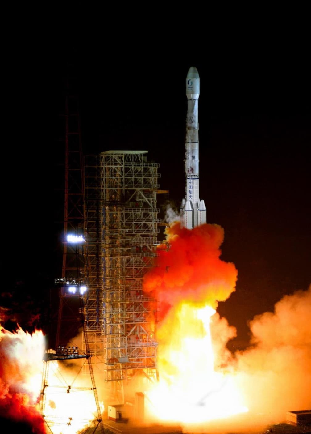 Čínská nosná raketa Dlouhý pochod 3B (CZ-3B) startuje v noci z obslužné věže v oblaku ohně a kouře; na těle jsou nápisy „CZ 3B" a „中国航天".
